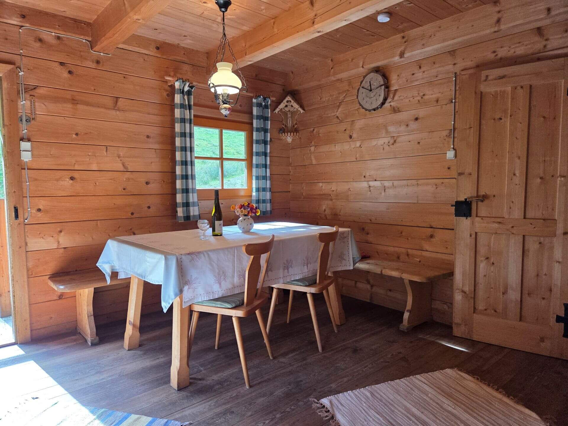 Der Esstisch in der Mühlenhütte mit einer Weinfalsche und Blumen als Dekoration.