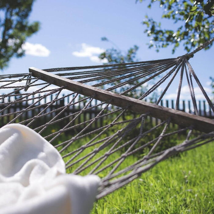 Zwischen zwei Bäumen in der Natur hängt die Hängematte und darauf liegt eine Kuscheldecke.