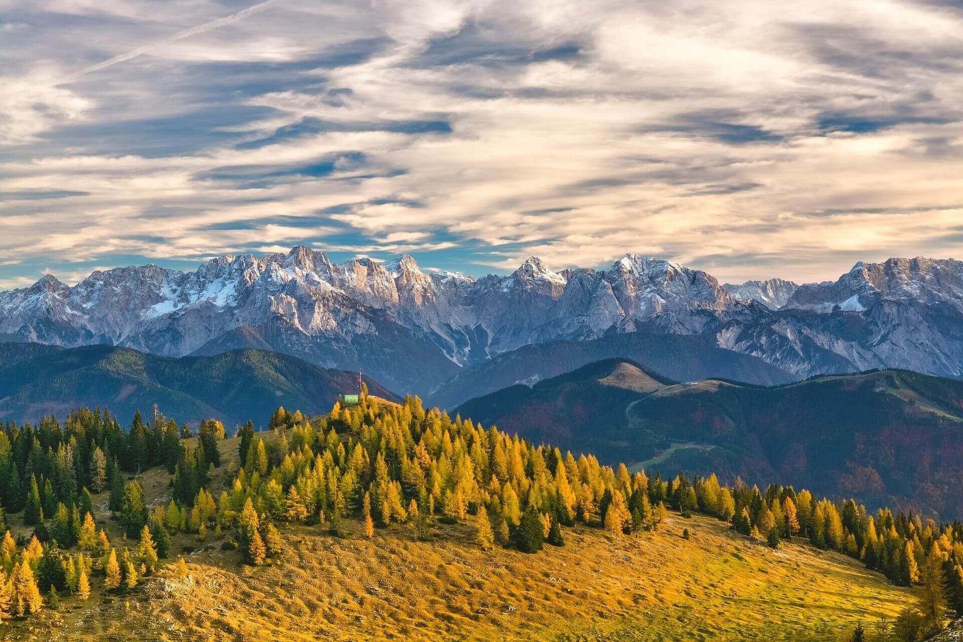 Weitläufiger Blick auf die Alpenkette bei Sonnenaufgang, mit goldenem Licht auf den Gipfeln.